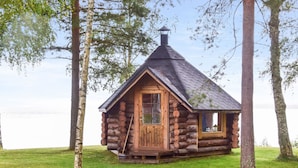 Une cabane en rondins avec un toit à forte pente, une cheminée et une fenêtre.