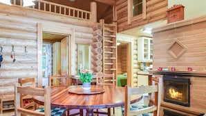 L’intérieur d’une cabane en rondins, avec une table à manger en bois, des chaises, une cheminée et un escalier.