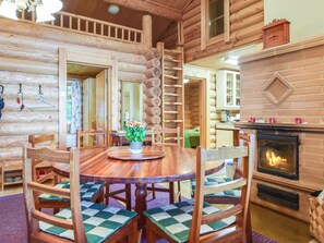 A log cabin interior with a wooden dining table, chairs, a fireplace, and a kitchen area. - Kivitasku by Interhome (Ikaalinen)