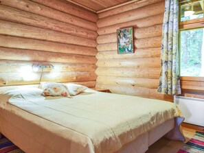 A log cabin bedroom with a bed, a painting on the wall, and a window with curtains.