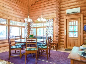 A log cabin interior with a round dining table surrounded by chairs, a chandelier, and a large window with curtains.