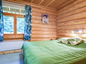 Un dormitorio de cabaña de madera con una cama, cortinas, una ventana y un cuadro en la pared.