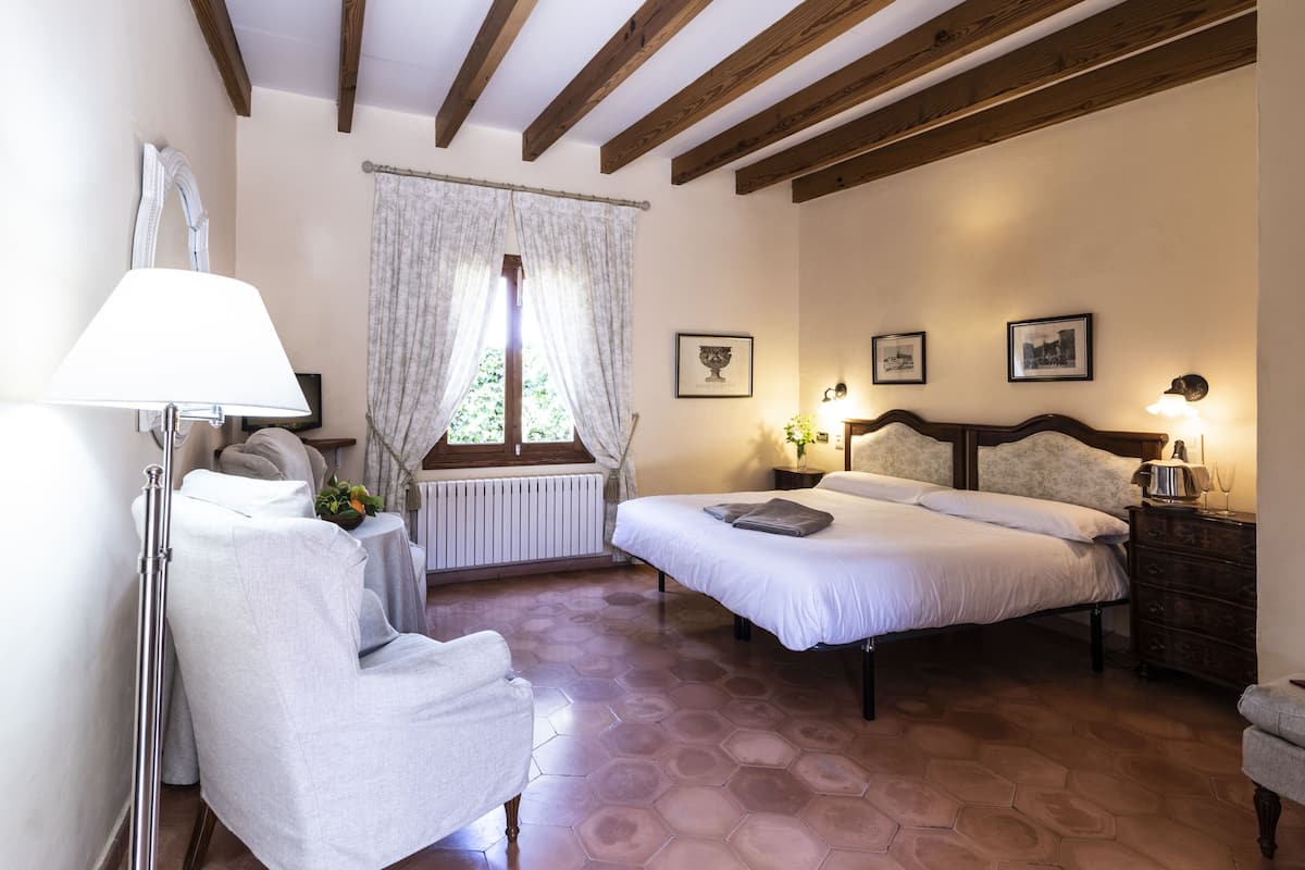 A bedroom with a bed, two bedside tables, a chair, a lamp, and a window with curtains.
