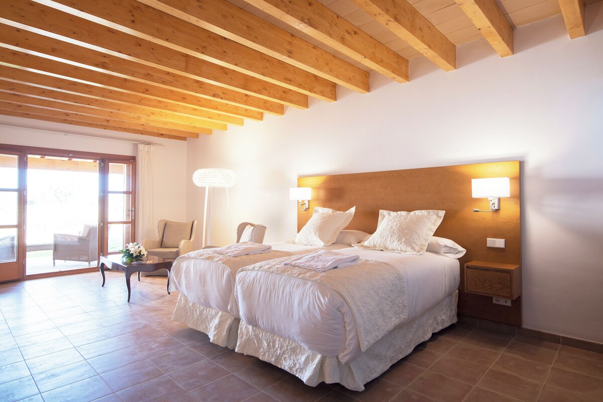 A bedroom with two beds, wooden beams, a nightstand, and a lamp.