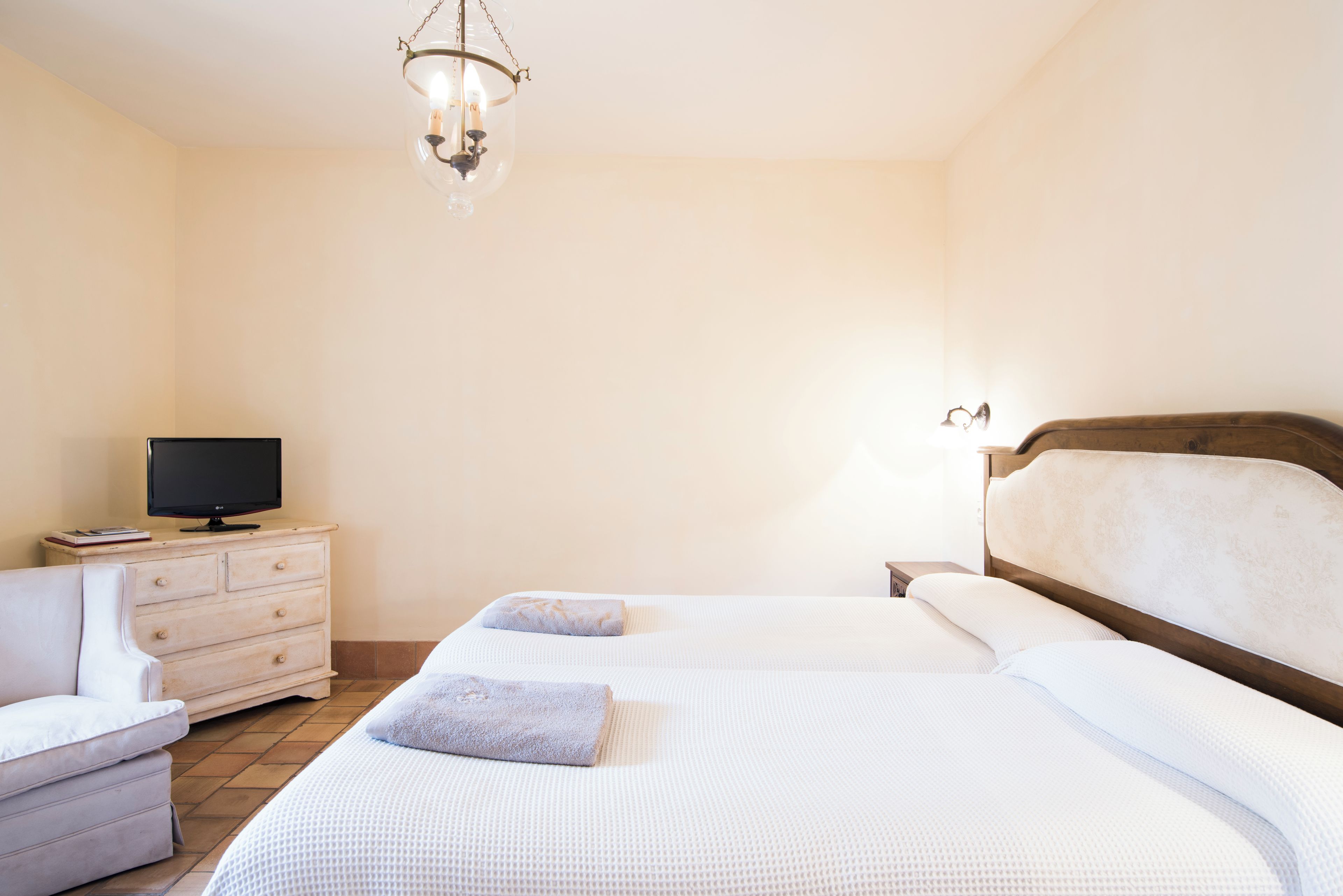 A hotel room with two beds, a TV on a dresser, a chair, and a chandelier.