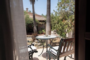 An outdoor patio with a round table and two chairs, surrounded by plants and trees.