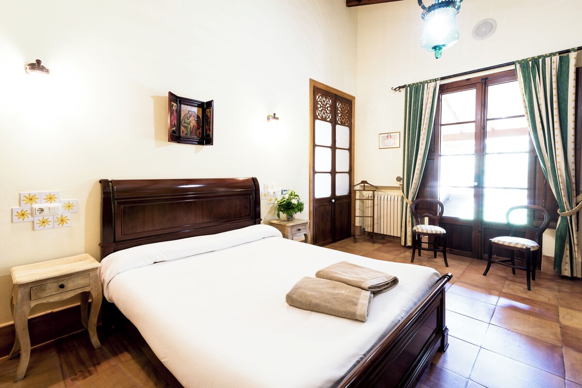A neatly made bed with a wooden headboard, a bedside table with a lamp, and a window with curtains.