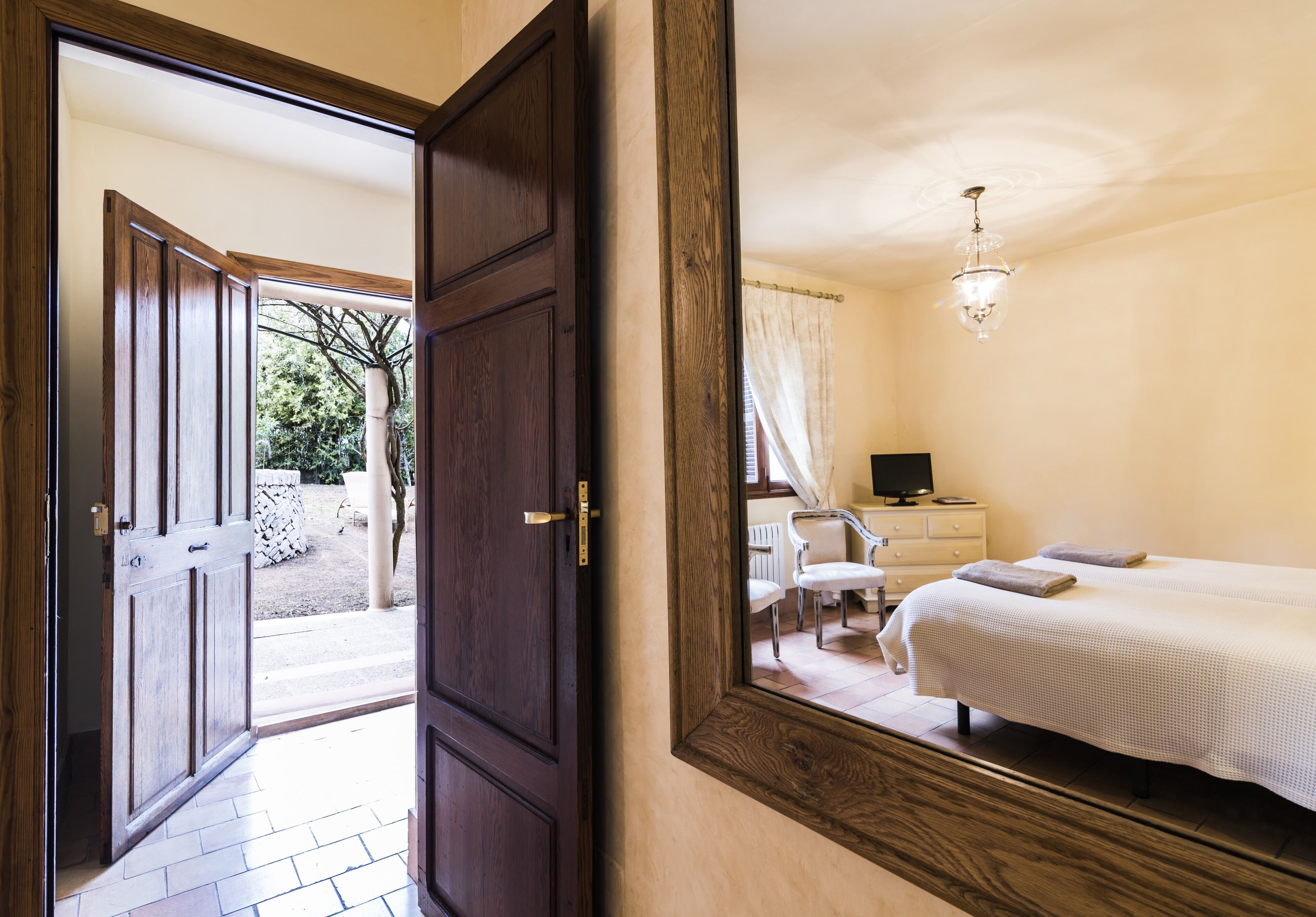 Hotelkamer met een grote spiegel die het interieur van de kamer reflecteert, een bed, een nachtkastje, een stoel en een raam met gordijnen.