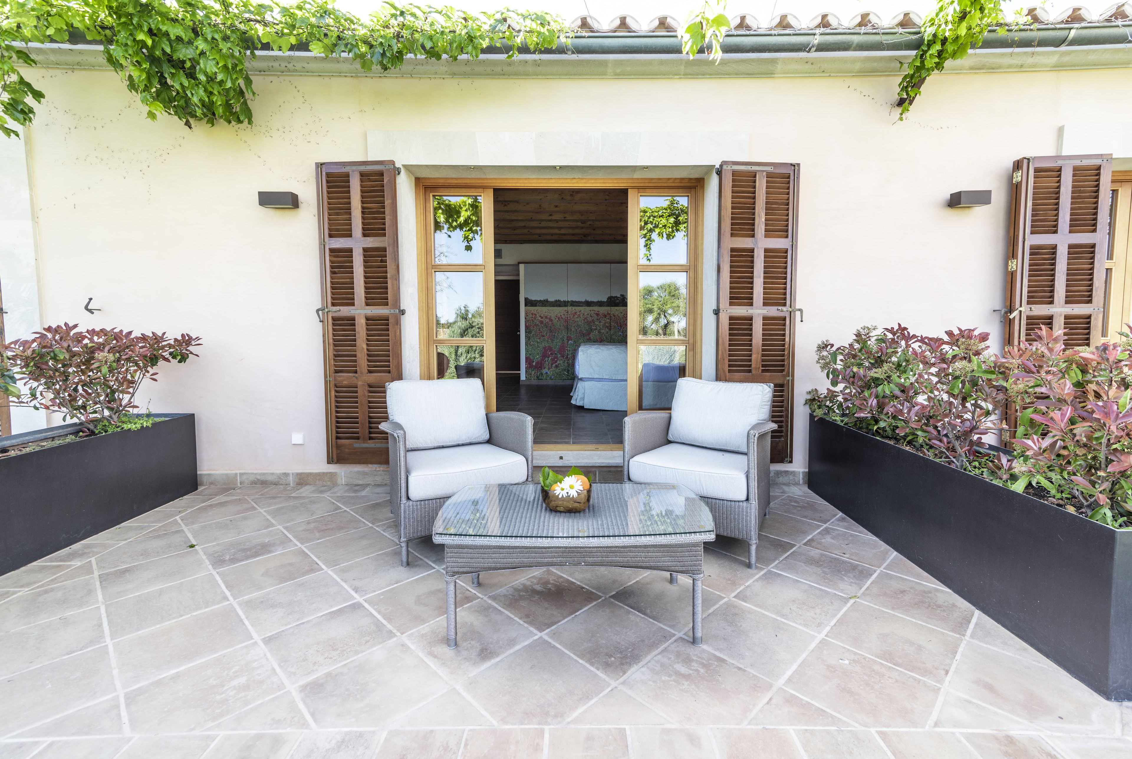 Un patio al aire libre con dos sillones blancos acolchados, una mesa con cubierta de vidrio y un pequeño arreglo floral.