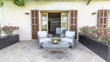 Un patio al aire libre con dos sillones blancos acolchados, una mesa con cubierta de vidrio y un pequeño arreglo floral.