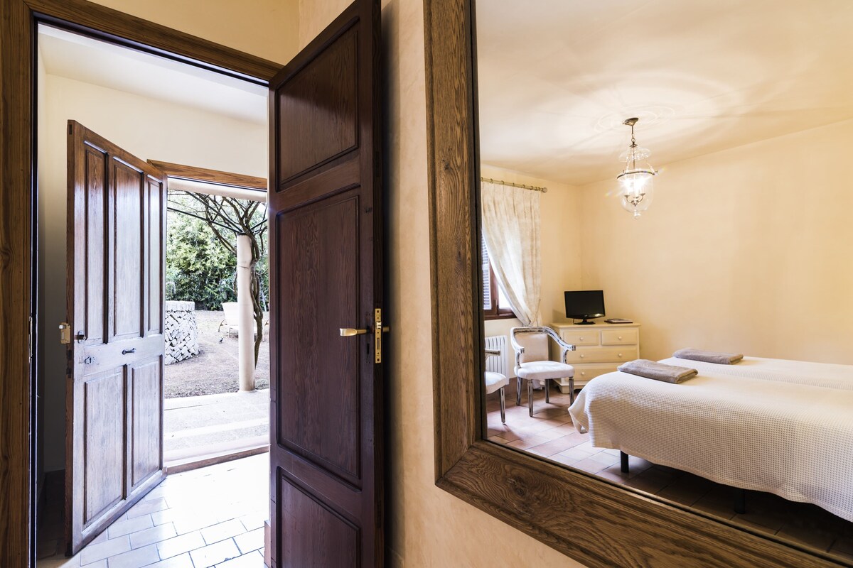 A hotel room with a large mirror, a bed, a desk, a chair, and a view of the outside.