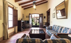Ein geräumiges Wohnzimmer mit einer großen Couch, einem Couchtisch und einem Bücherregal. Durch einen offenen Durchgang ist ein Gartenblick möglich.