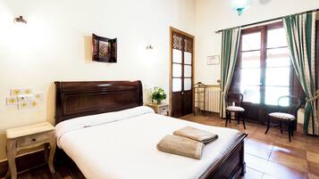Una cama bien hecha con cabecera de madera, una mesita de noche con lámpara y una ventana con cortinas.