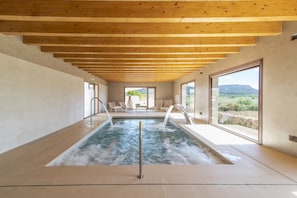 A spa area with a hot tub, wooden ceiling beams, and large windows offering a view of the outdoors. - Aumallia Hotel & Spa (Felanitx)