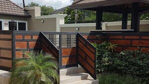 A gated entrance with a staircase leading to a covered area, surrounded by greenery and a residential building in the background. - The Penthouse at Comfort Living (Kingston)
