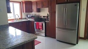 A kitchen with wooden cabinets, a stainless steel refrigerator, a microwave, and an oven. - The Penthouse at Comfort Living (Kingston)