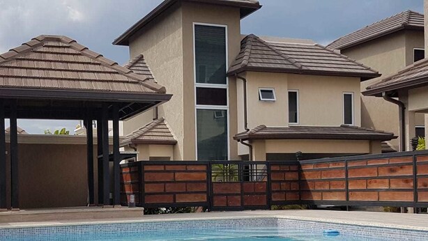 A swimming pool with a tiled deck, a gazebo, and a brick wall. - The Penthouse at Comfort Living (Kingston)