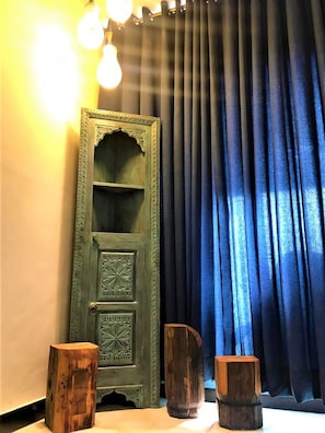 A room with a green door, a blue curtain, and three wooden stools. - Roomy ISB Atlas (Islamabad)