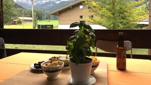 Una mesa con planta en maceta, aperitivos en recipientes y una botella, con vista a la montaña al fondo.