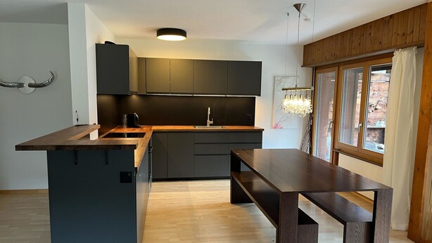 Una cocina moderna con armarios oscuros, una isla de madera y un comedor con banco.