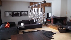 Una sala de estar moderna con un sofá de cuero negro, una mesa de centro de madera, una chimenea y una araña.