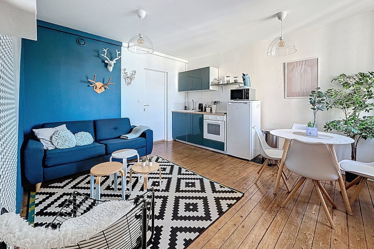Un appartement moderne avec un canapé bleu, un coin repas, une cuisine et un tapis à motifs.
