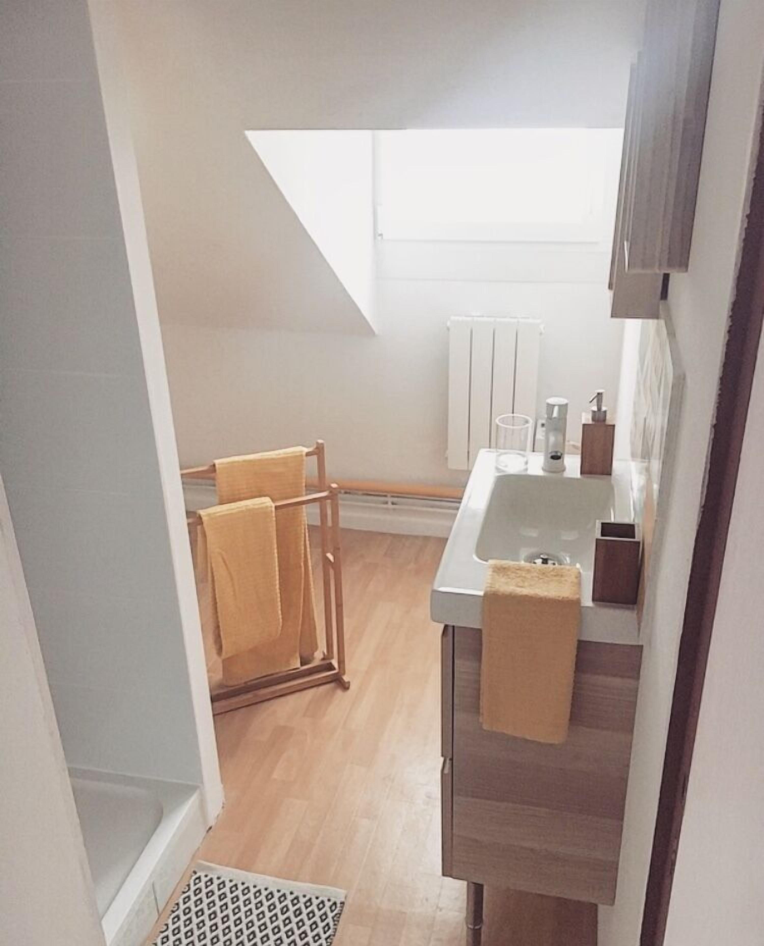 A narrow, well-lit kitchen with a wooden floor, a white sink, and a towel rack.