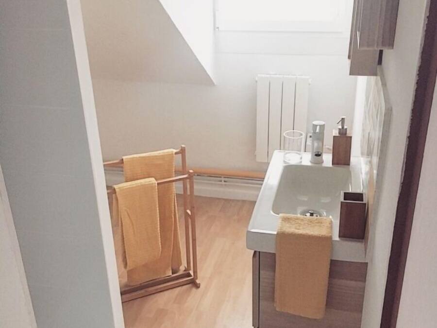A narrow, well-lit kitchen with a wooden floor, a white sink, and a towel rack.