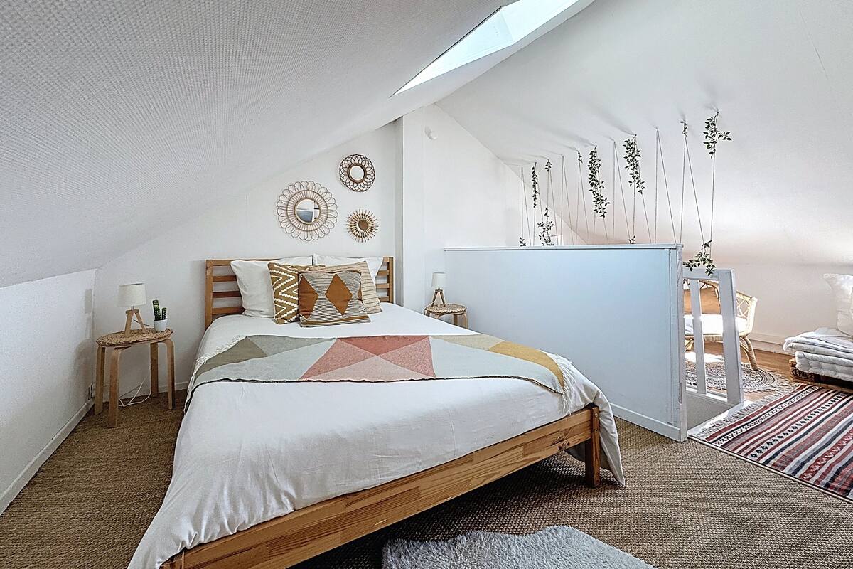 Une chambre avec un plafond en pente, un lit avec une literie à motifs, une table de chevet avec une lampe et des décorations murales.