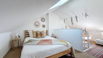 Un dormitorio con techo inclinado, una cama con ropa de cama estampada, una mesita de noche con lámpara y adornos en la pared.