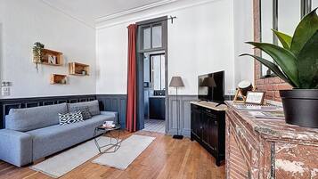 Sala de estar moderna com um sofá cinzento, piso de madeira, uma TV sobre um suporte de madeira e um vaso com planta.