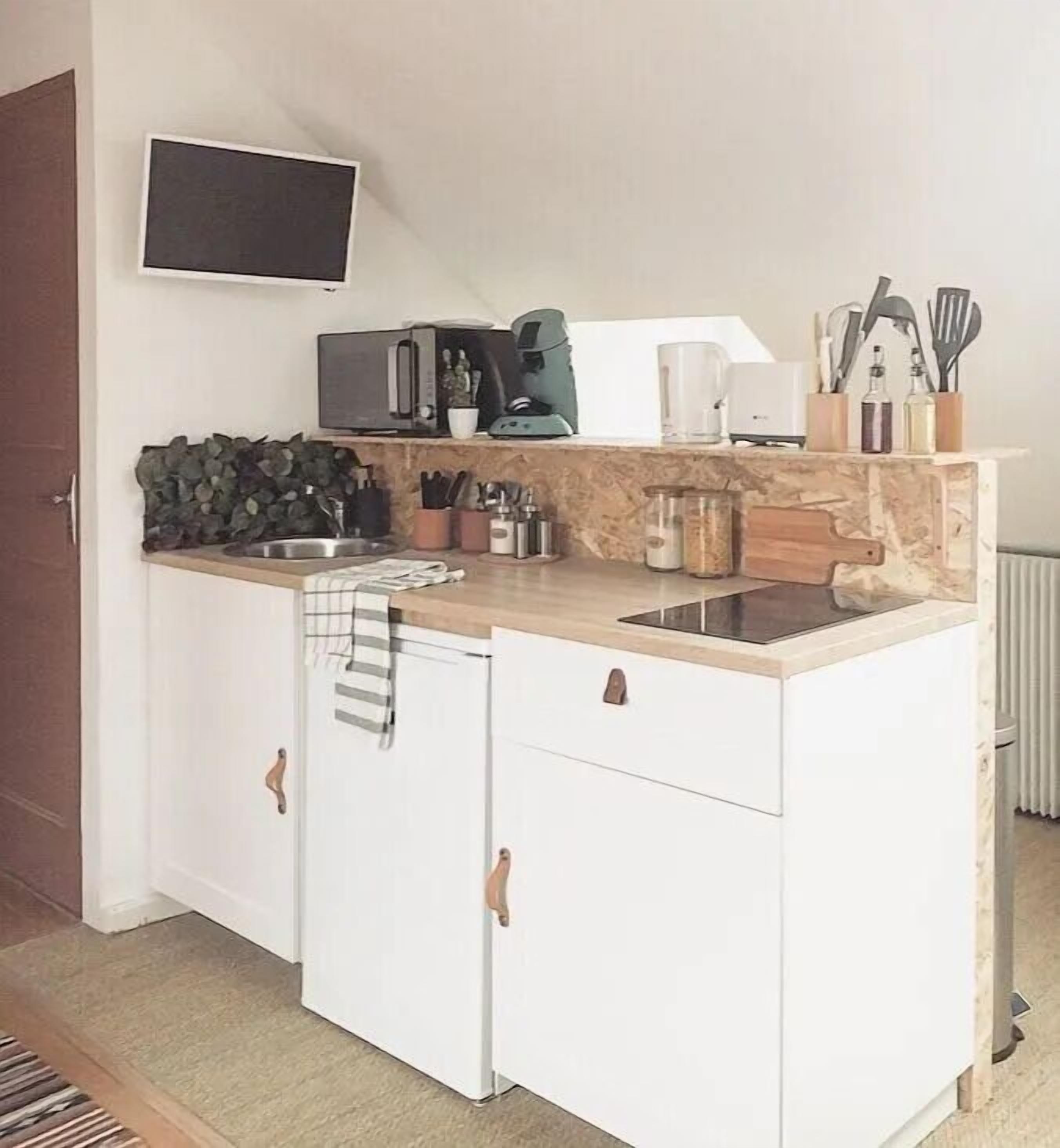 A compact kitchen with a built-in stove, a microwave, and a coffee maker. There are cabinets with wooden handles and a small sink.