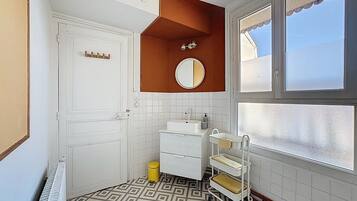 Un baño con puerta y lavamanos blancos, un espejo, un perchero para toallas y una ventana.