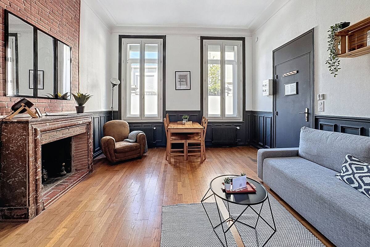 Un salon avec une cheminée, un canapé, une table à manger et deux fenêtres.