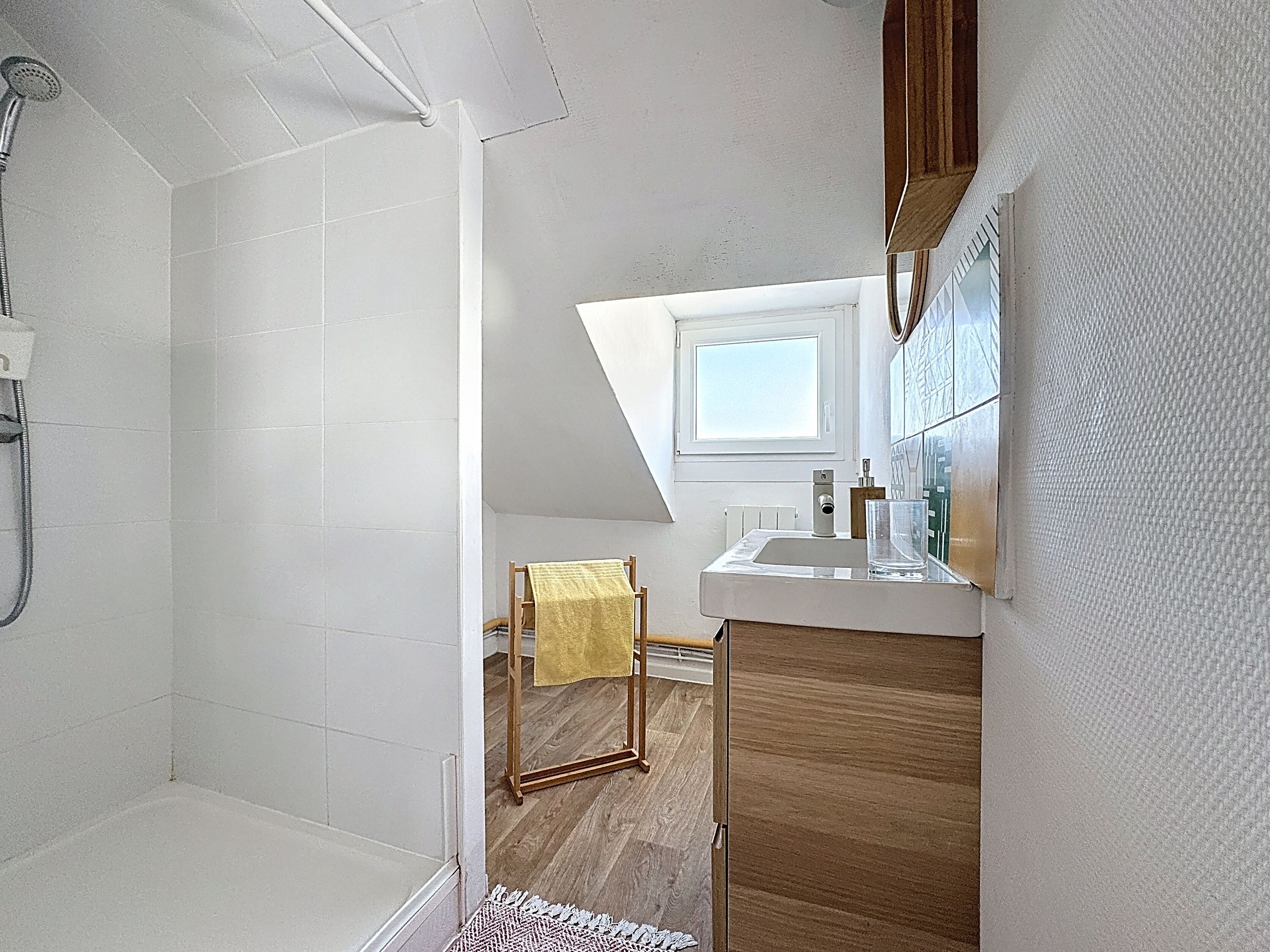 A modern bathroom with a shower, a small window, and a wooden floor.