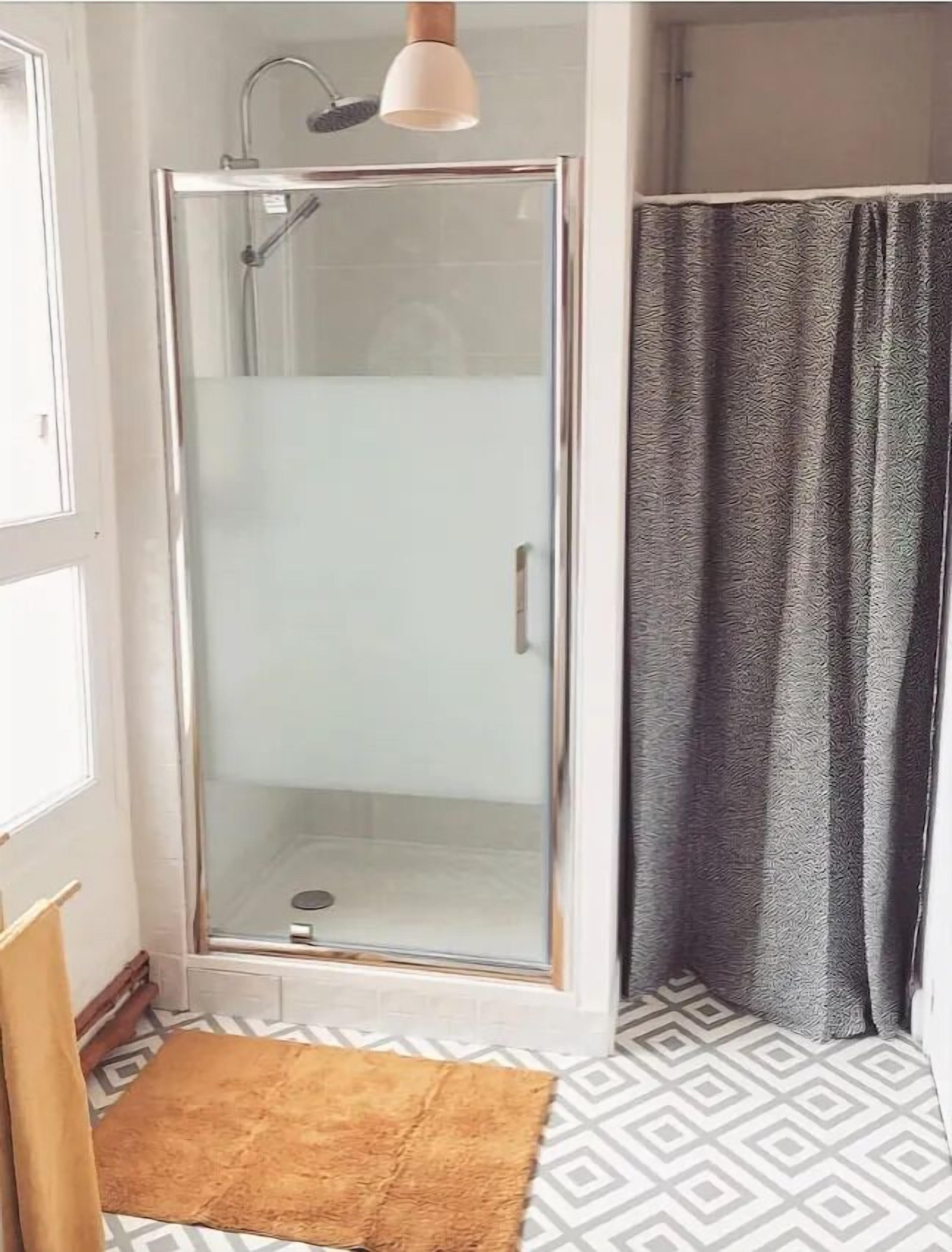 Une douche fermée par des parois en verre, dotée d’un pommeau de douche à main, d’un porte-serviettes et d’un carrelage décoratif.