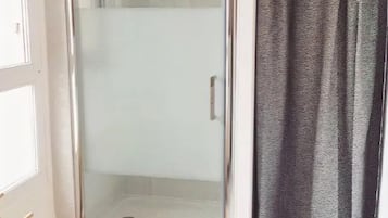 Une douche fermée par des parois en verre, dotée d’un pommeau de douche à main, d’un porte-serviettes et d’un carrelage décoratif.
