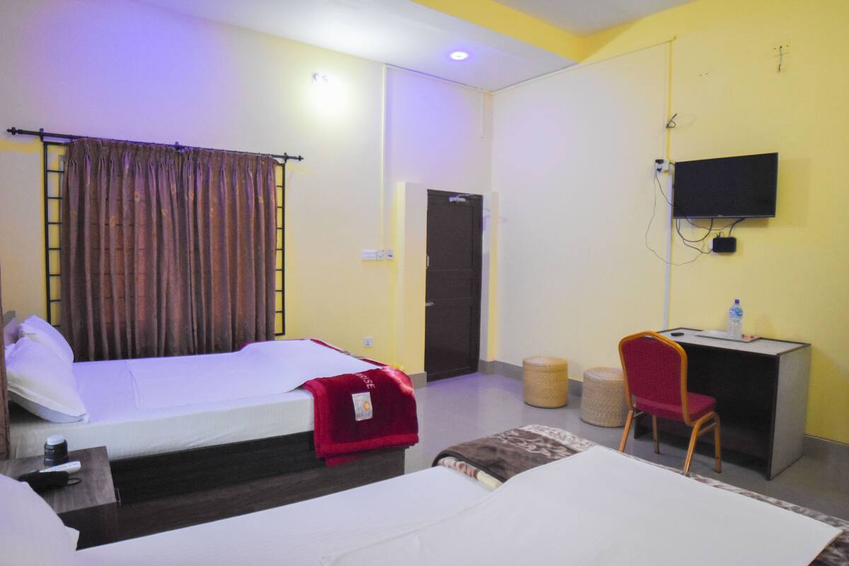 A hotel room with two beds, a desk with a chair, a television, and a door.