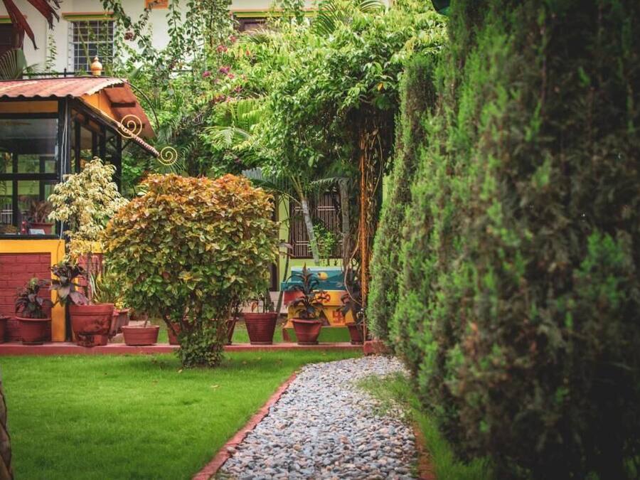 A garden with a gravel path, potted plants, and a building with a red roof.
