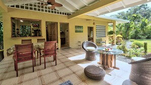 Un patio couvert comprenant un coin repas, des chaises, une table et un ventilateur de plafond.
