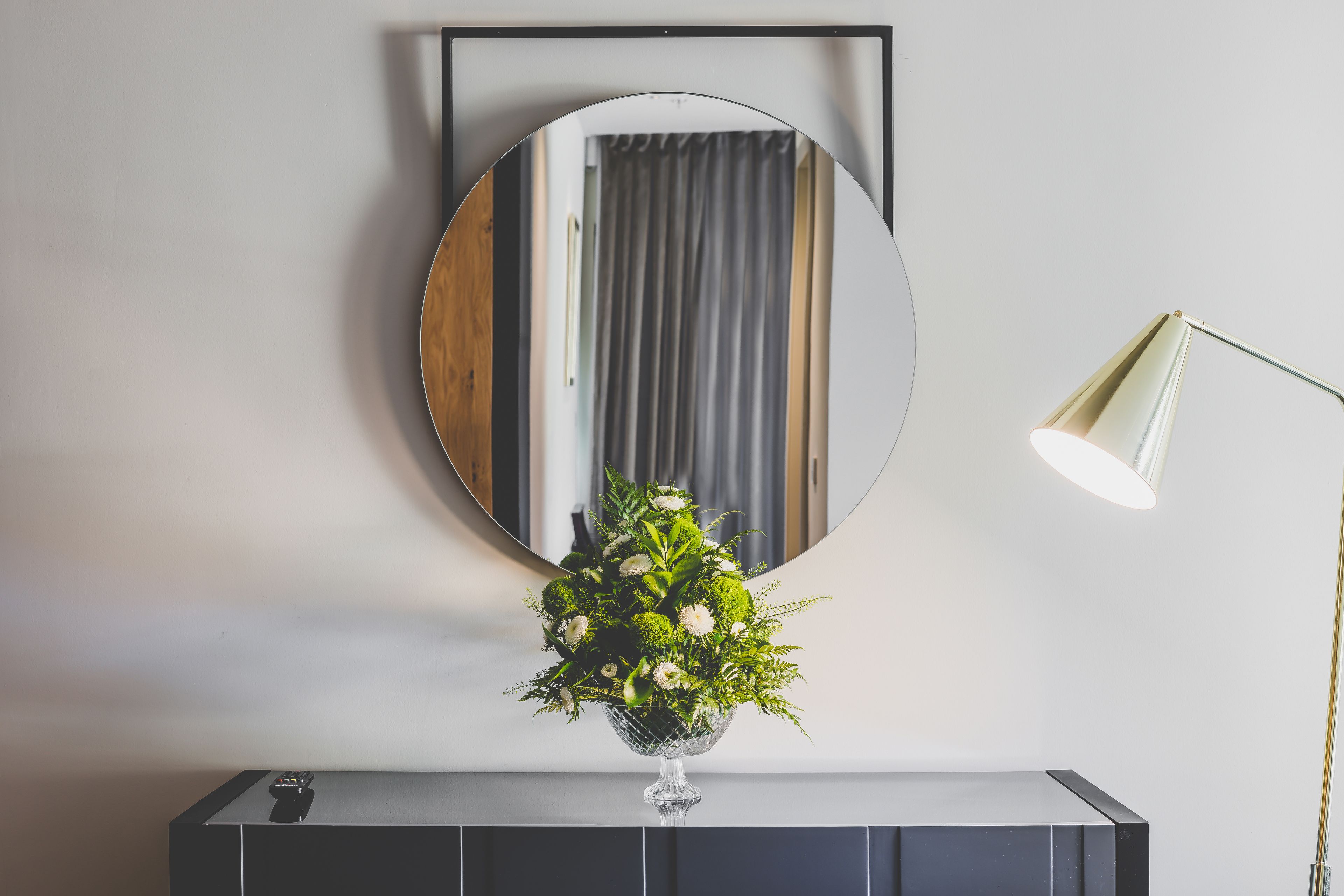 Una habitación moderna con un espejo redondo, un florero con flores y una lámpara.