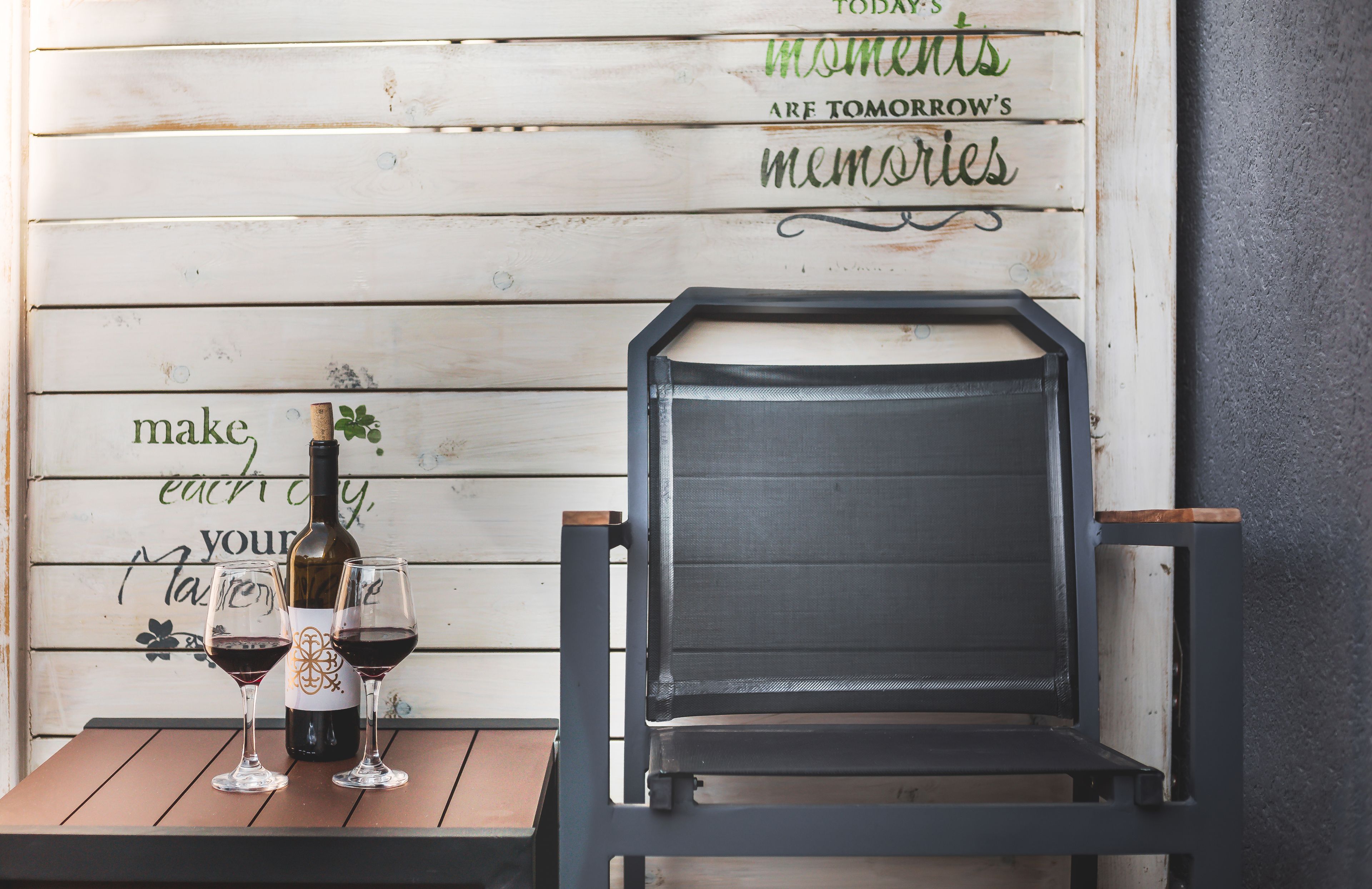 A wooden wall with a motivational quote, a wine bottle, and two glasses on a wooden table.
