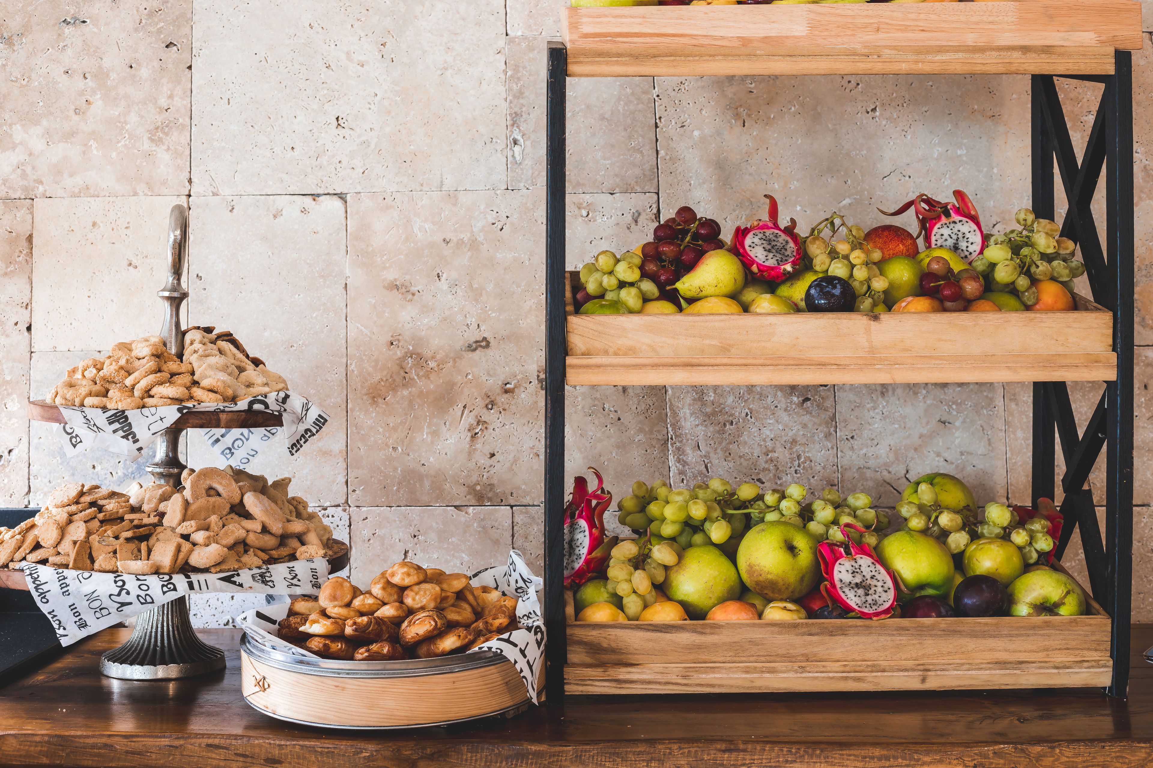 A wooden fruit and cookie display with a tiled wall background.
