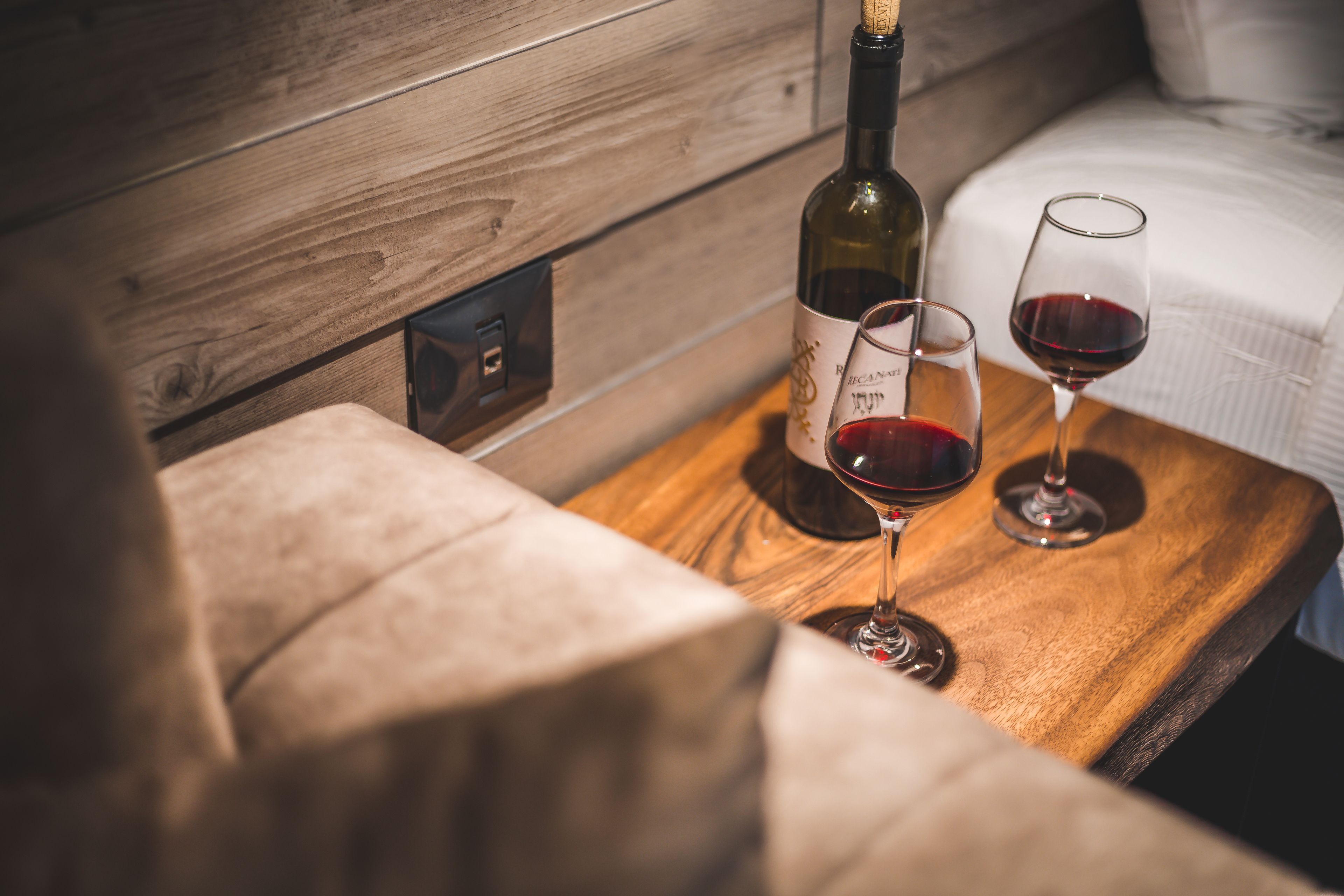 Una mesa de madera con una botella de vino y dos copas de vino tinto.