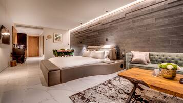 A modern bedroom with a curved bed, a sofa, a wooden coffee table, and a stone wall.