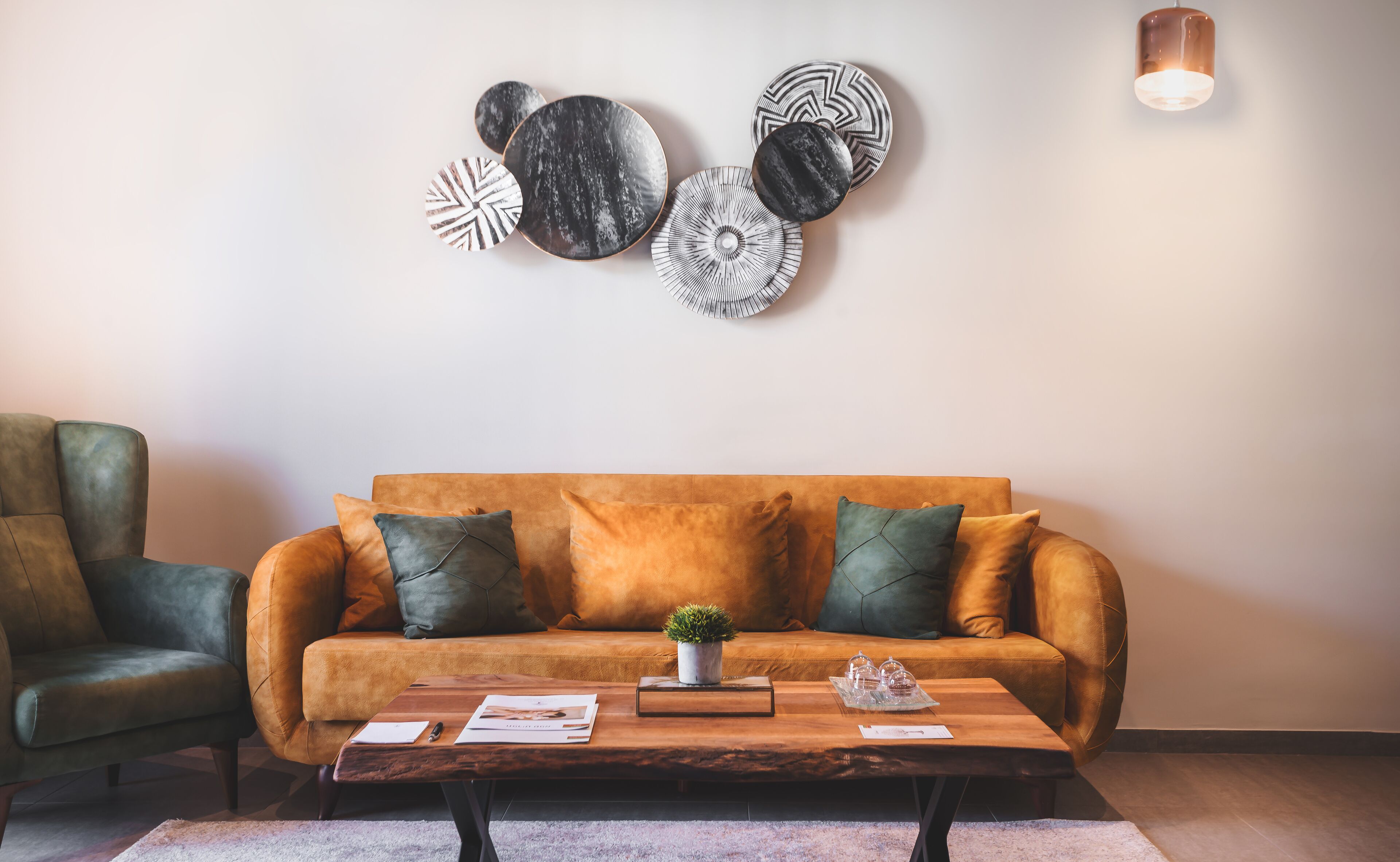 Una sala de estar con un sofá marrón, cojines verdes, una mesa de centro con una planta y obras de arte en la pared.