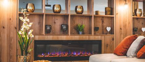 Una sala de estar acogedora con chimenea, estantes de madera con objetos decorativos, un sofá y una mesa de centro.