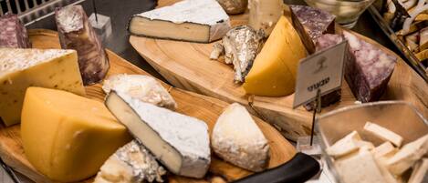 A variety of cheeses on a wooden board with a knife and a bowl of olives in the background.