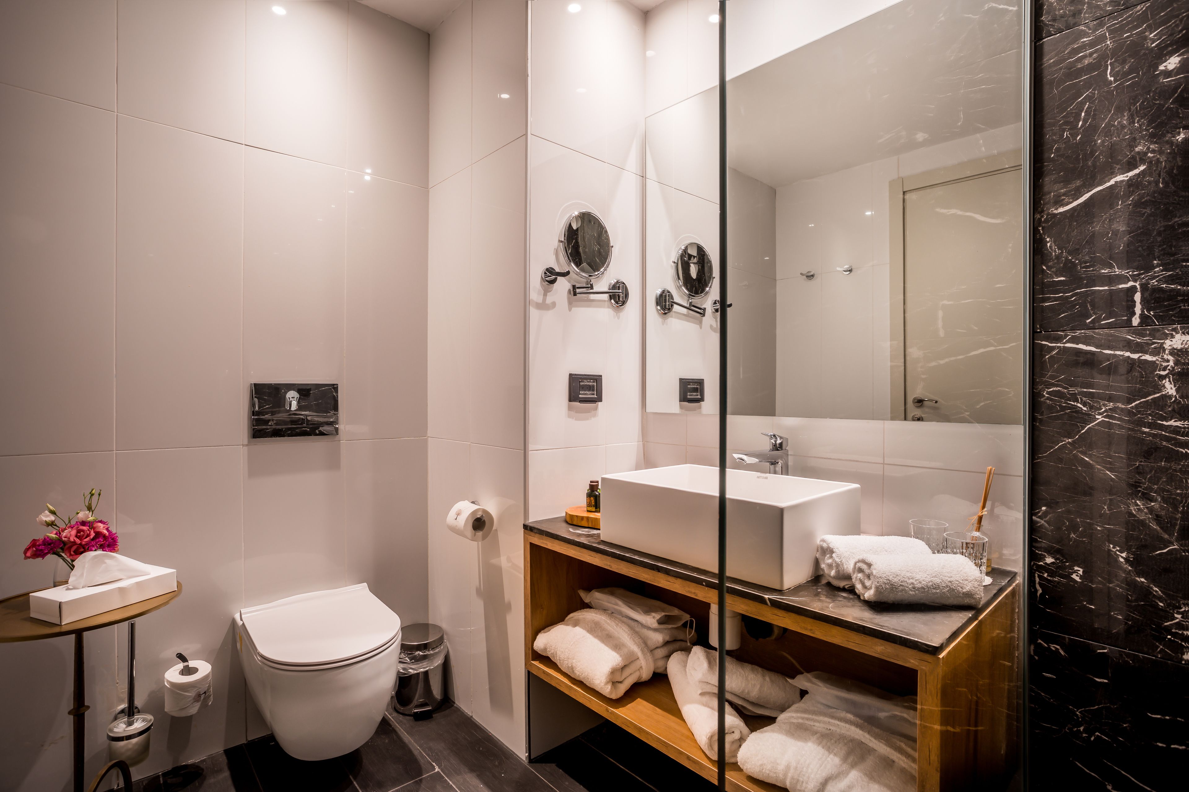 Un baño moderno con inodoro blanco, ducha con mampara de vidrio, tocador con lavabo blanco y espejo.