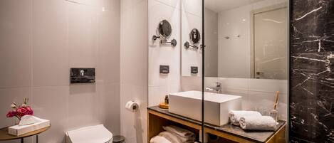 Un baño moderno con inodoro blanco, ducha con mampara de vidrio, tocador con lavabo blanco y espejo.